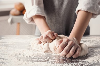 Photo of Woman kneading dough at table in kitchen, closeup