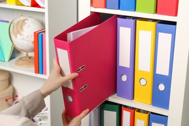 Photo of Woman taking binder office folder from shelving unit, closeup