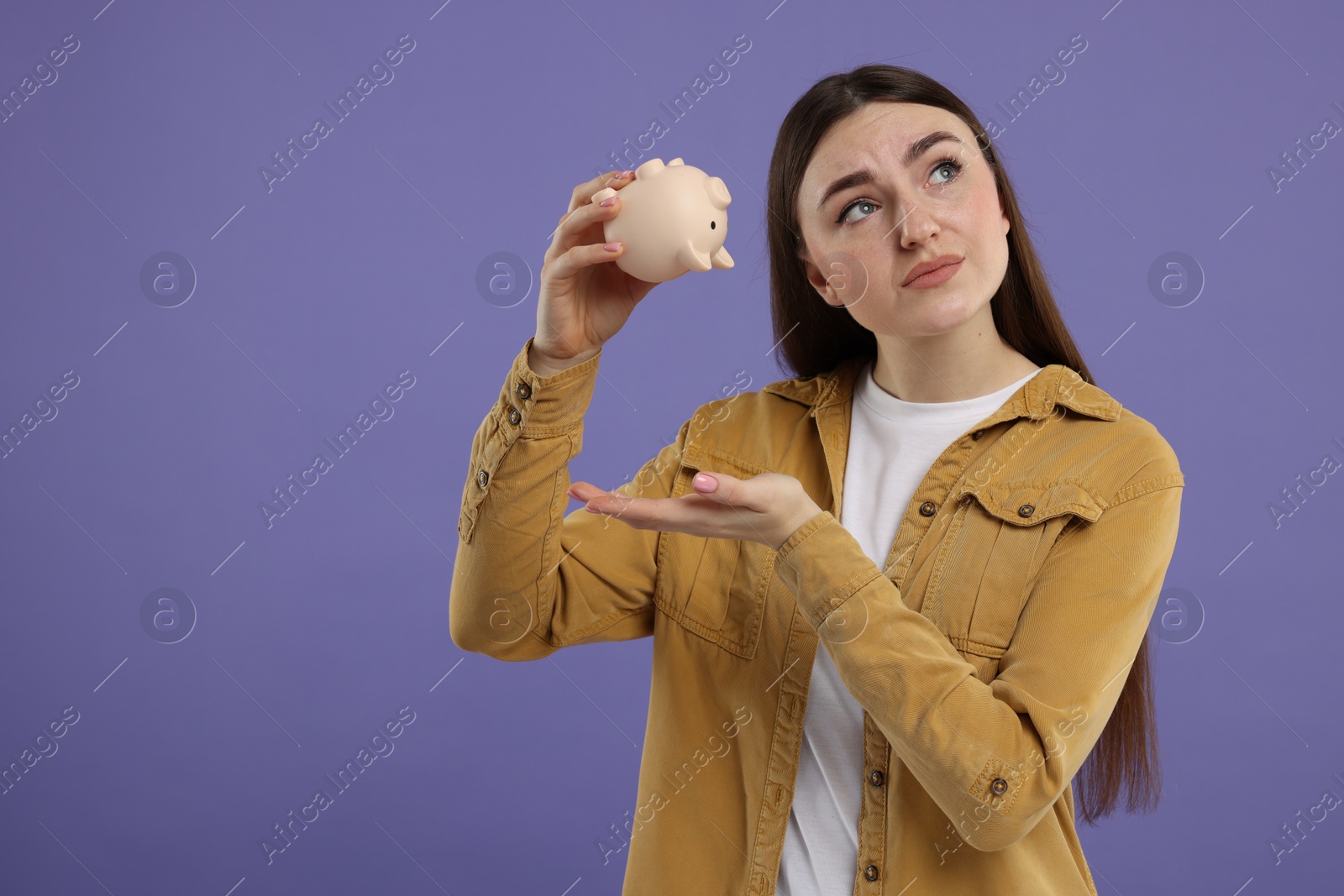 Photo of Sad woman with piggy bank on purple background, space for text