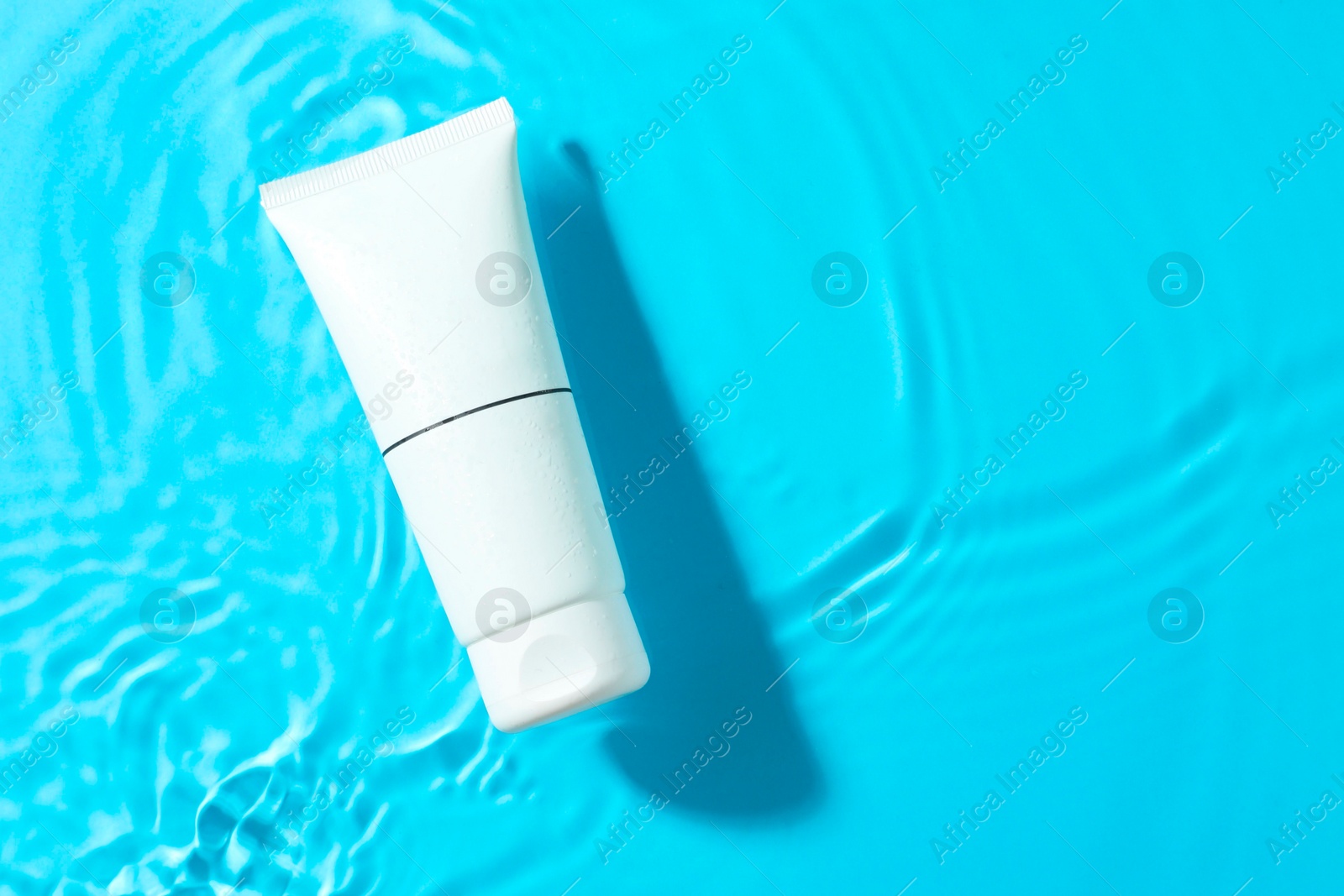 Photo of Tube with moisturizing cream in water on light blue background, top view. Space for text