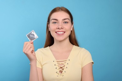 Photo of Woman holding condom on turquoise background. Safe sex