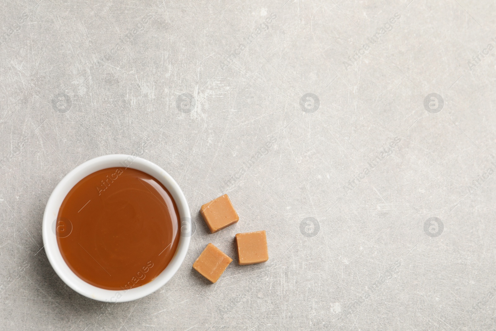 Photo of Yummy salted caramel in bowl and candies on grey table, flat lay. Space for text