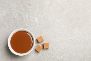 Photo of Yummy salted caramel in bowl and candies on grey table, flat lay. Space for text