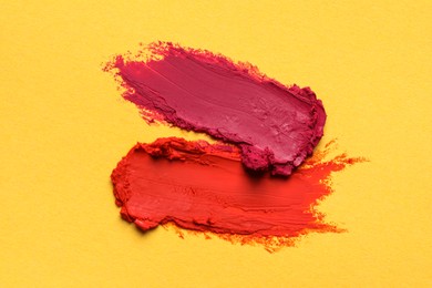 Photo of Smears of bright lipsticks on yellow background, top view