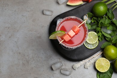 Cocktail glass of delicious fresh watermelon juice, lime, mint and ice on grey table, flat lay. Space for text