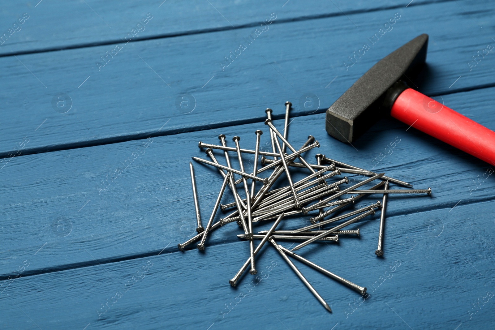 Photo of Hammer and metal nails on blue wooden table, space or text