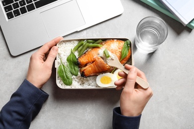 Woman eating natural protein food from container at office table, top view