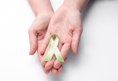 World Mental Health Day. Woman holding green ribbon on white background, top view
