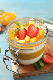 Photo of Delicious panna cotta with mango coulis and fresh fruit pieces on light blue wooden table