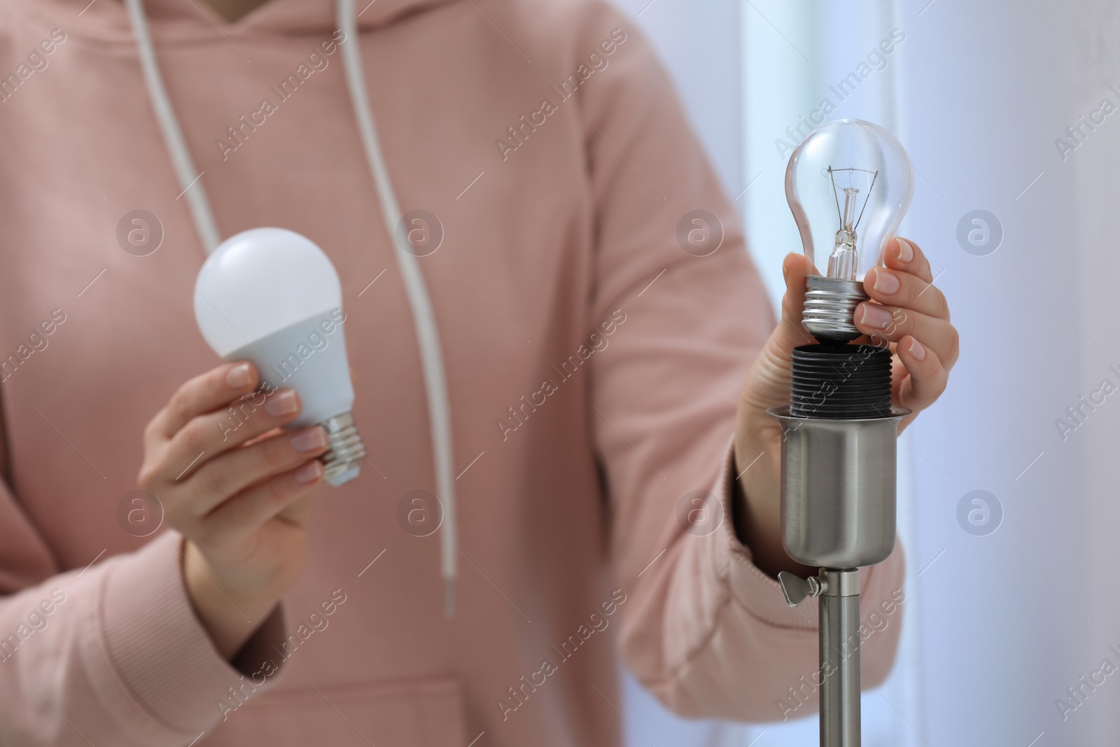 Photo of Woman changing incandescent light bulb for fluorescent one in lamp at home, closeup. Saving energy concept