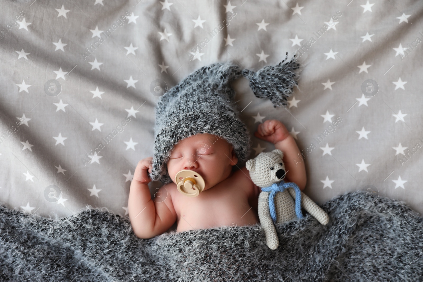 Photo of Cute newborn baby in warm hat with toy sleeping on bed, top view