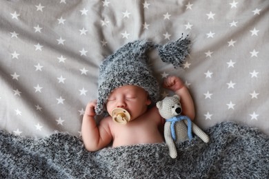 Cute newborn baby in warm hat with toy sleeping on bed, top view