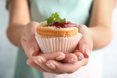 Woman with delicious plum cupcake on light background, closeup