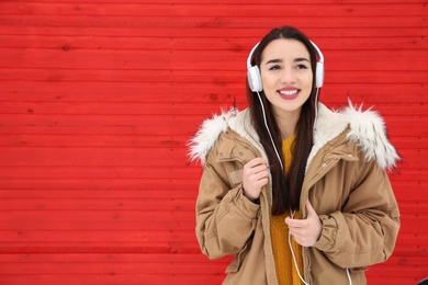 Photo of Beautiful young woman listening to music with headphones against color wall. Space for text
