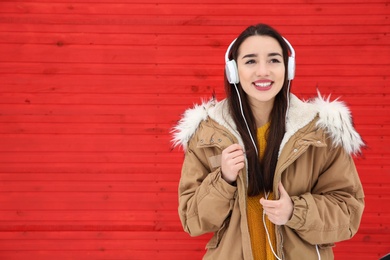 Beautiful young woman listening to music with headphones against color wall. Space for text