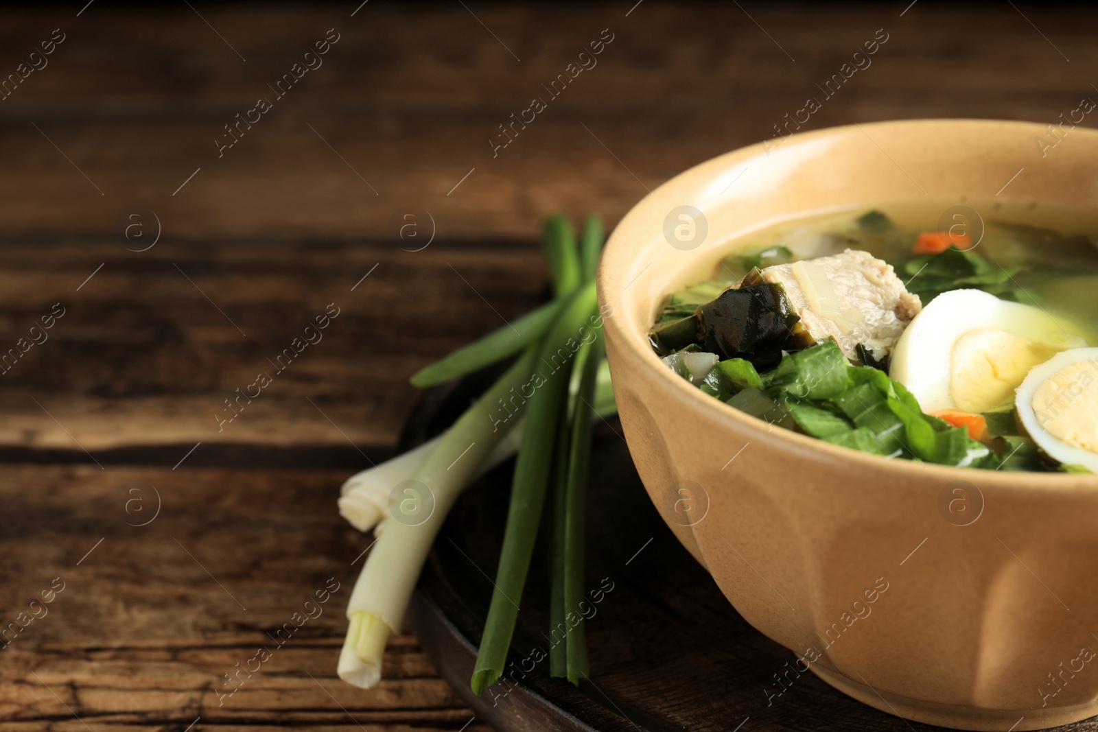 Photo of Delicious sorrel soup with meat and eggs served on wooden table, closeup. Space for text