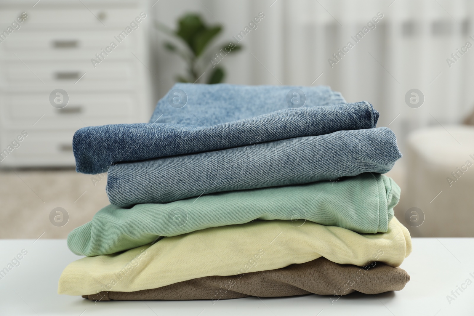 Photo of Stack of different folded clothes white on table, closeup