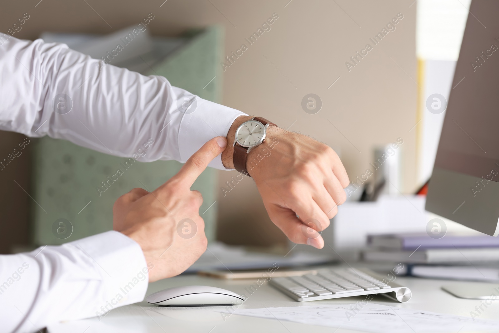 Photo of Young man checking time on his wristwatch at workplace