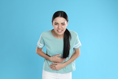 Photo of Woman suffering from stomach ache on light blue background. Food poisoning