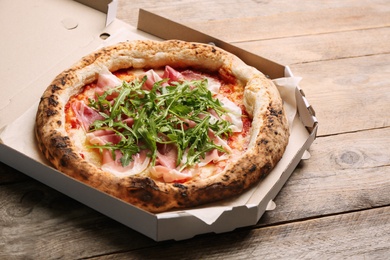 Tasty pizza with meat and arugula in cardboard box on wooden table