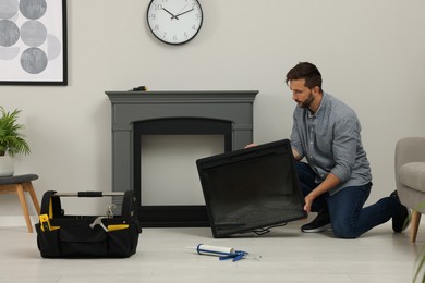 Man installing electric fireplace near wall in room