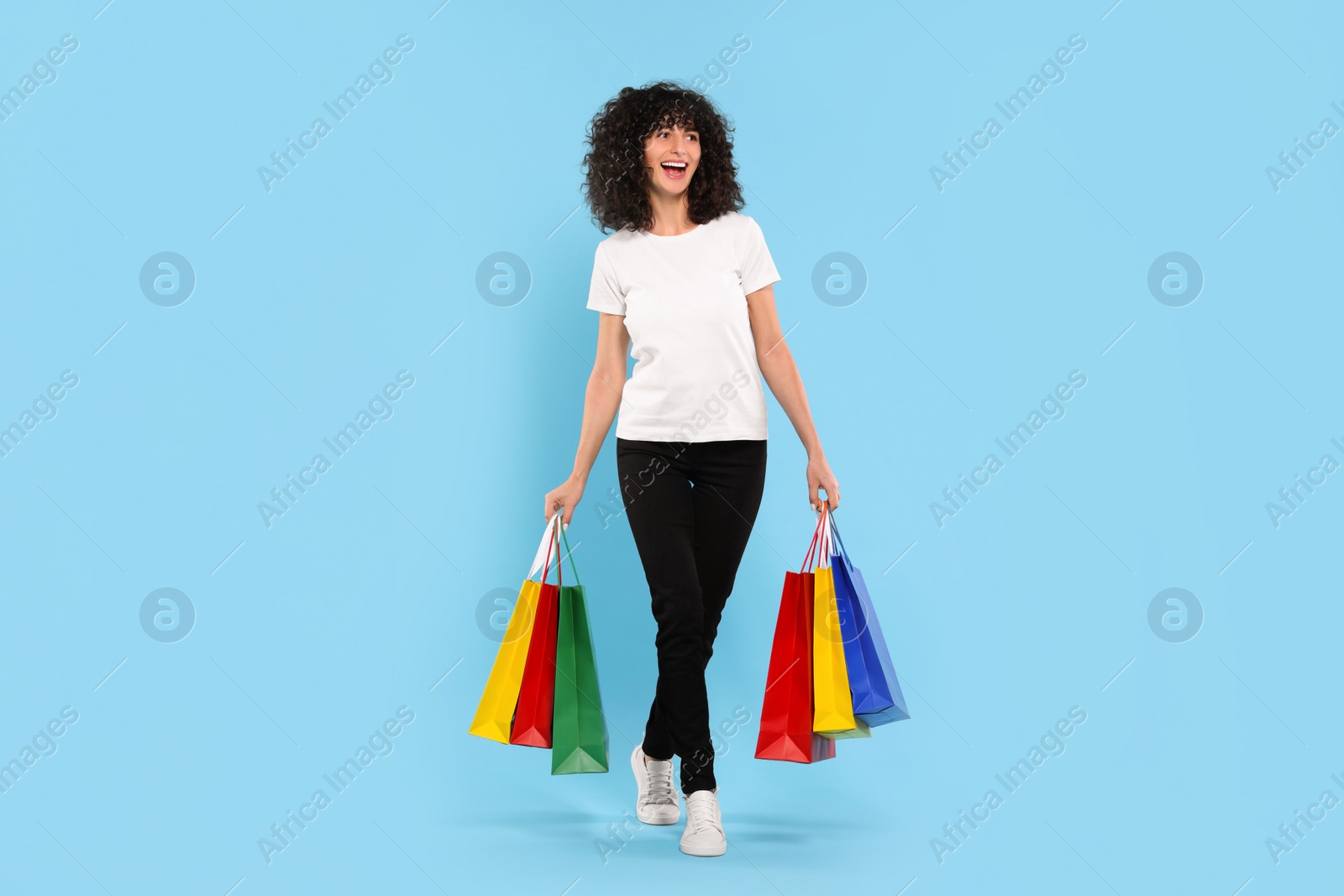 Photo of Happy young woman with shopping bags on light blue background