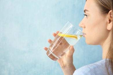 Photo of Young woman drinking water with lemon against color background