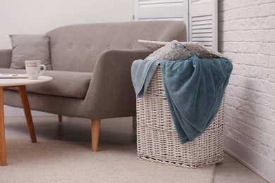 Basket with blankets and pillow near sofa indoors