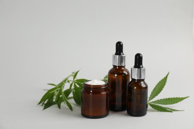 Photo of Cream, hemp leaves, bottles of CBD oil and THC tincture on light grey background. Space for text