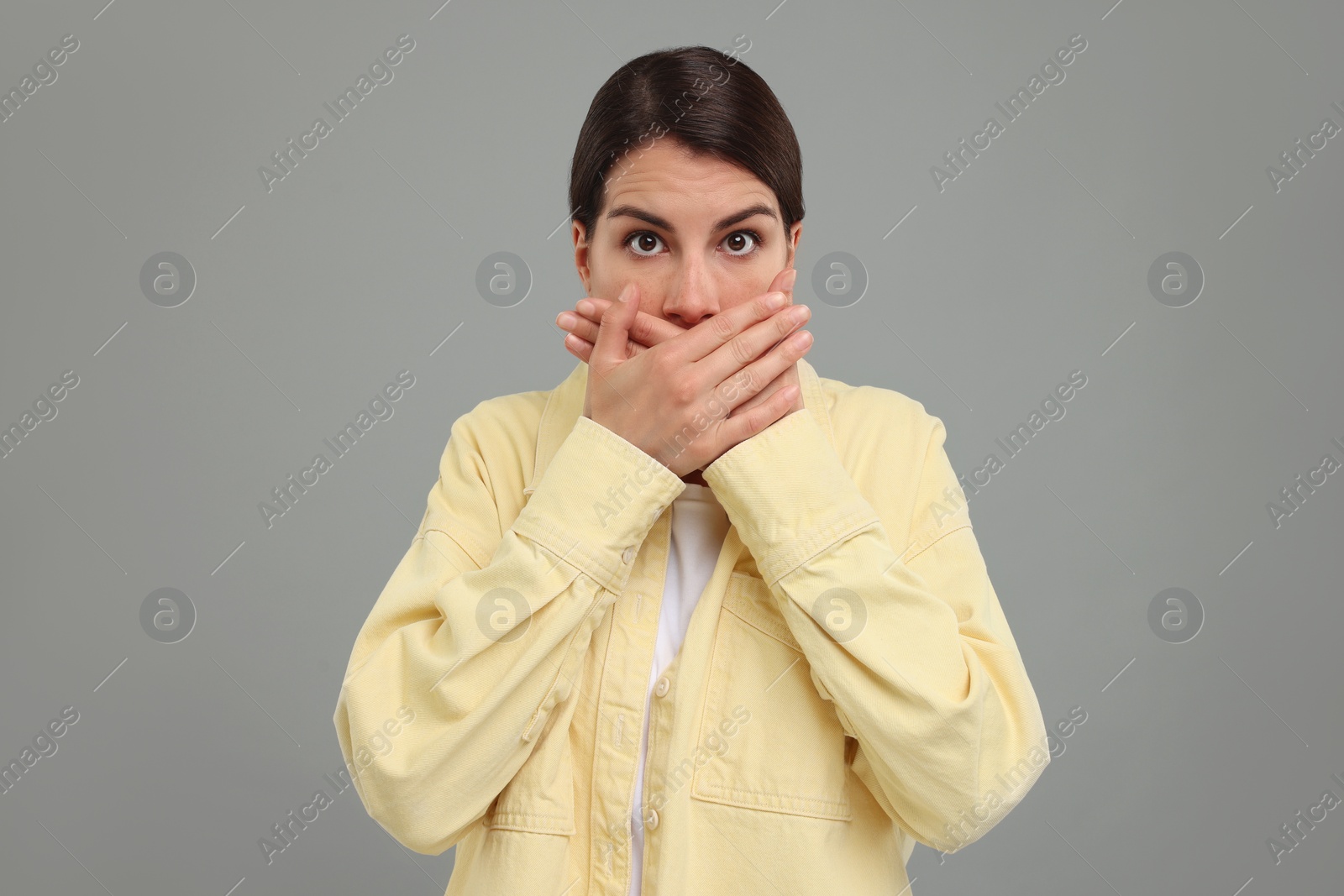 Photo of Embarrassed woman covering mouth with hands on grey background