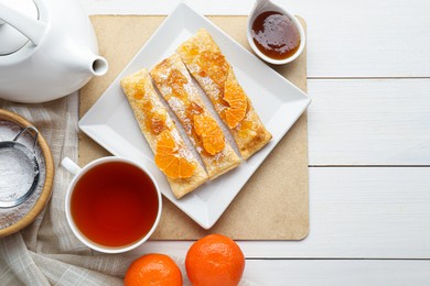 Fresh tasty puff pastry with sugar powder, jam and tangerines served on white wooden table, flat lay. Space for text