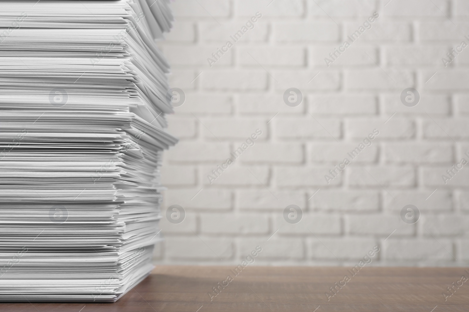 Photo of Stack of paper sheets on wooden table near white brick wall, space for text