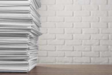 Stack of paper sheets on wooden table near white brick wall, space for text