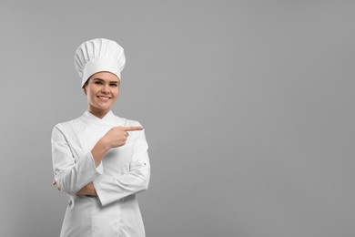 Happy female chef pointing at something on light grey background. Space for text