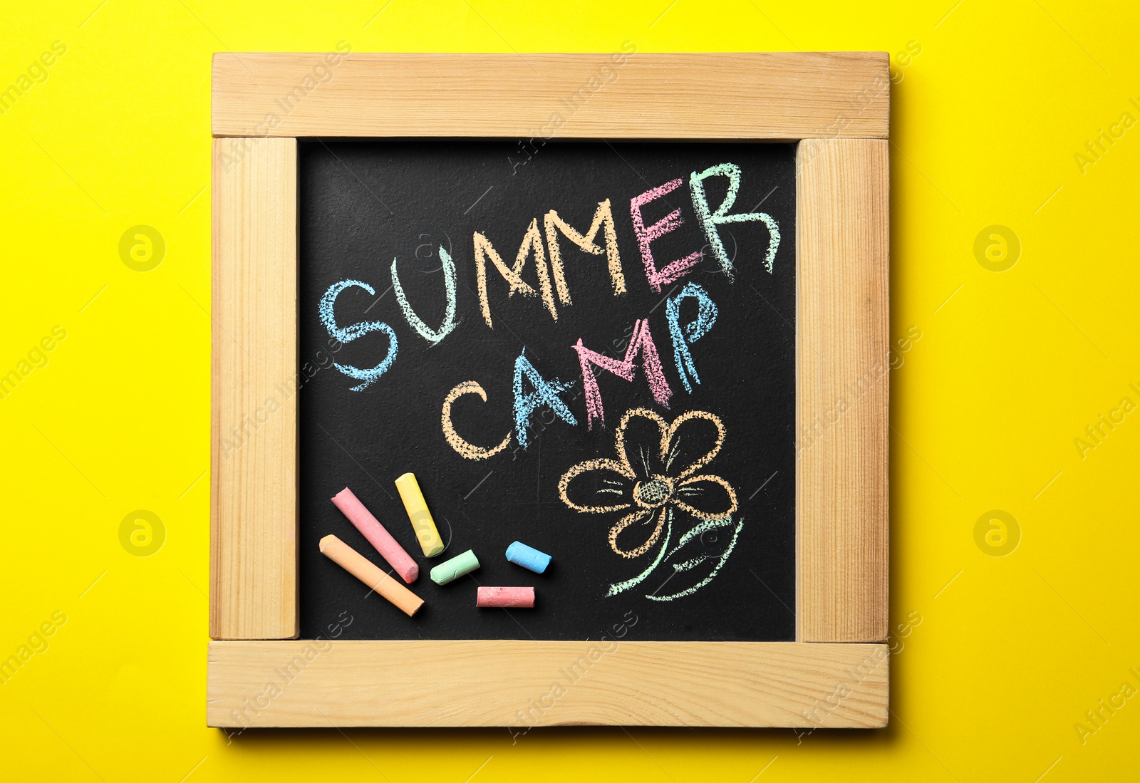 Photo of Small blackboard with text SUMMER CAMP, drawing and chalk sticks on color background, top view