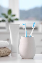 Photo of Plastic toothbrushes in holder, toothpaste and towels on white table indoors
