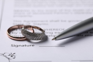 Photo of Marriage contract, pen and wedding rings, closeup