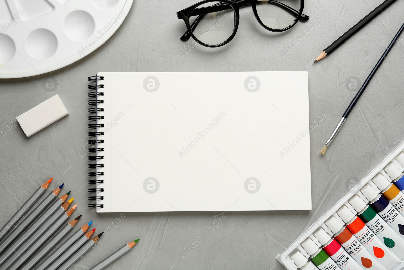 Photo of Flat lay composition with blank sketchbook on light grey stone table. Space for text