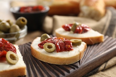 Photo of Delicious bruschettas with ricotta cheese, sun dried tomatoes and olives on table, closeup