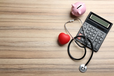 Photo of Flat lay composition with calculator and stethoscope on wooden background, space for text. Health insurance concept