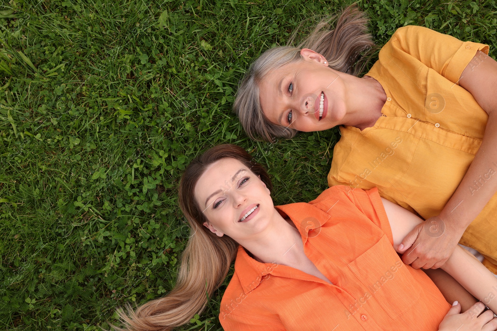 Photo of Happy mature mother and her daughter lying on green grass, top view. Space for text