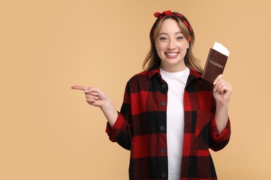 Happy young woman with passport and ticket pointing at something on beige background, space for text