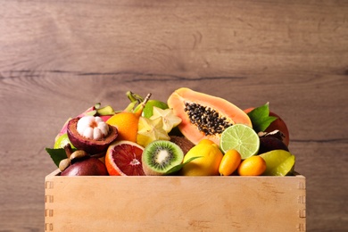Photo of Different tropical fruits in box on wooden background, closeup
