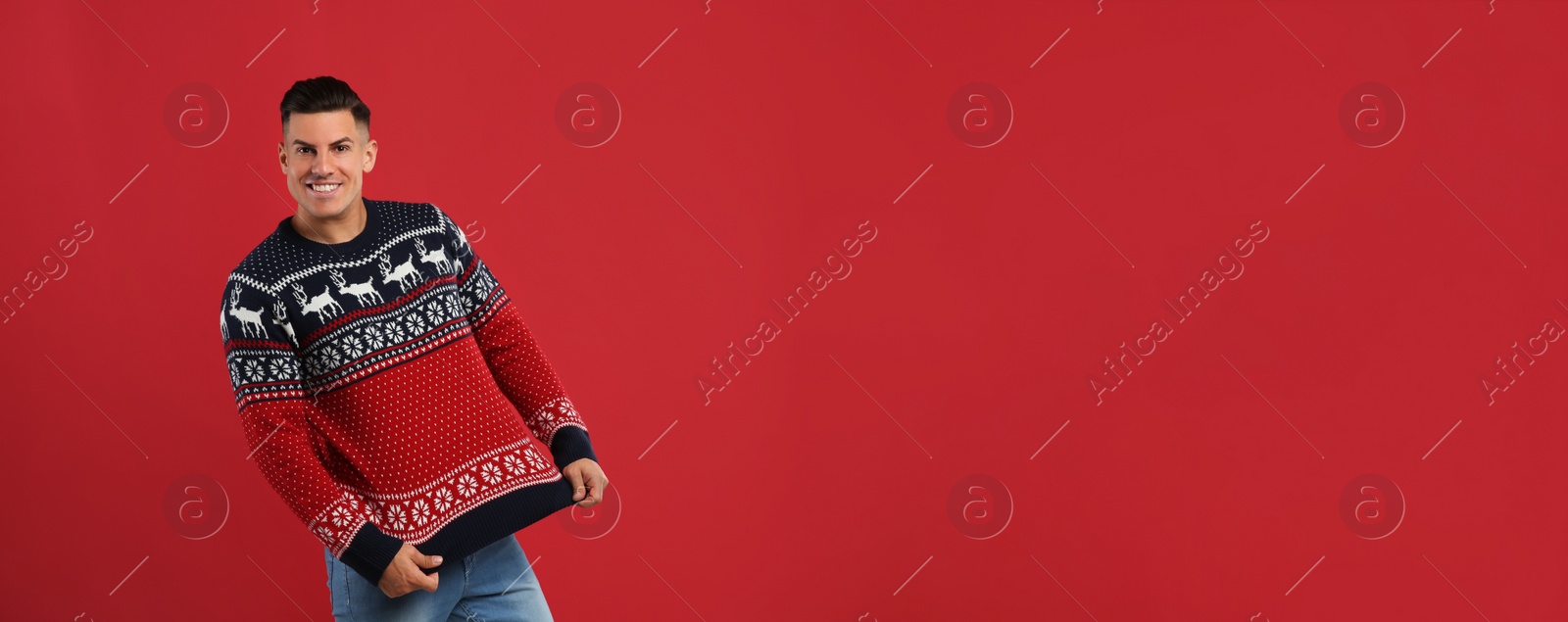 Photo of Happy man showing his Christmas sweater on red background