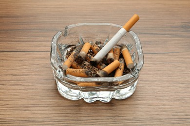 Photo of Glass ashtray with cigarette stubs on wooden table