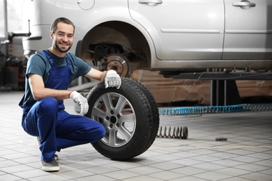 Photo of Young mechanic with car tire in service center