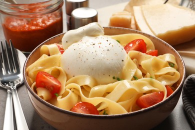Photo of Bowl of delicious pasta with burrata and tomatoes on grey table, closeup