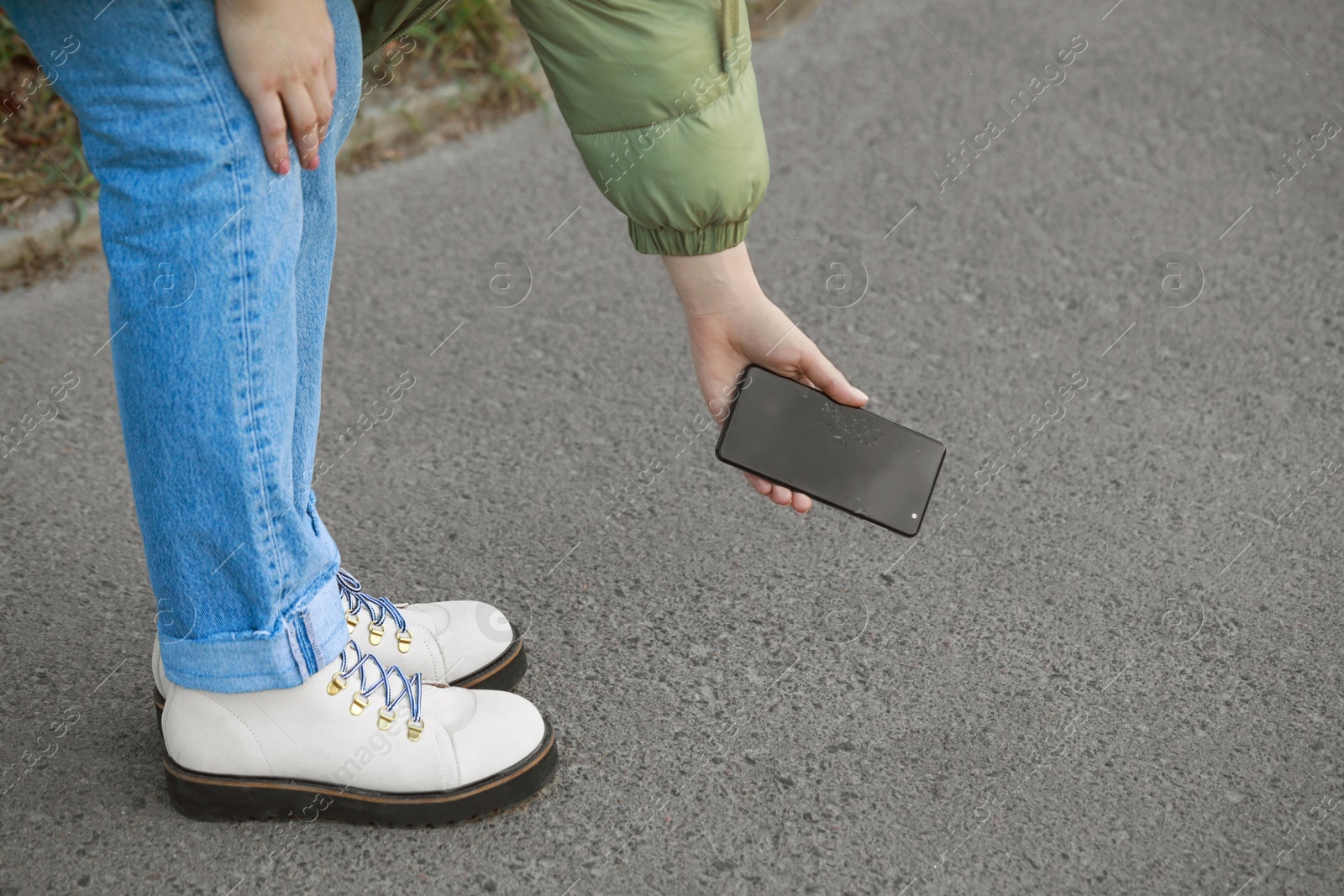 Photo of Woman taking dropped smartphone from asphalt outdoors, closeup. Device repairing