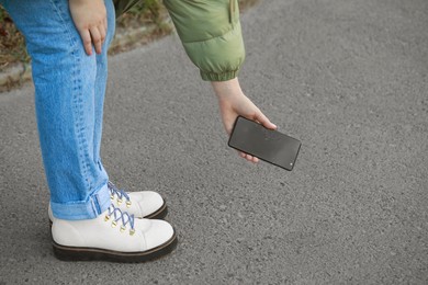 Woman taking dropped smartphone from asphalt outdoors, closeup. Device repairing