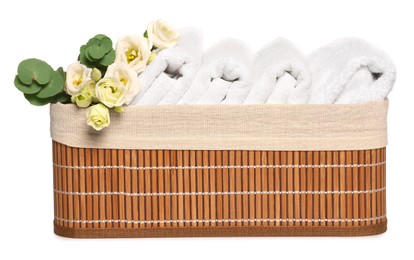 Photo of Wicker basket with folded soft terry towels, flowers and eucalyptus branch on white background